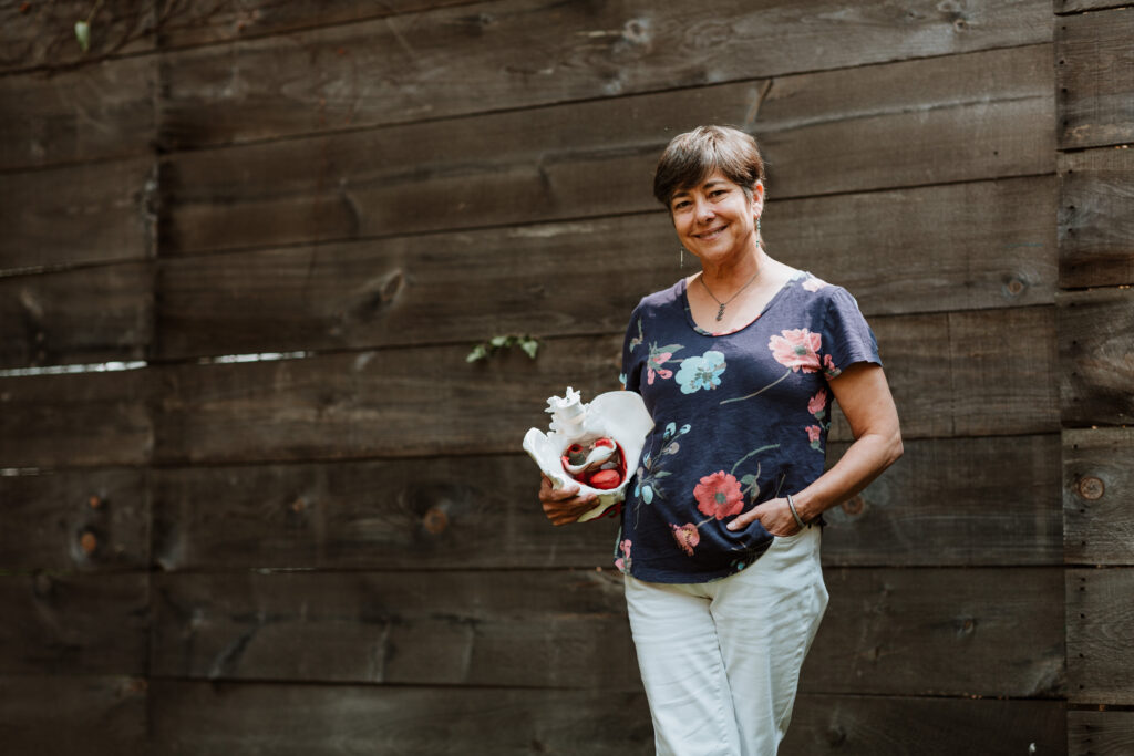 woman therapist standing by a wooden wall holding pelvis skeleton