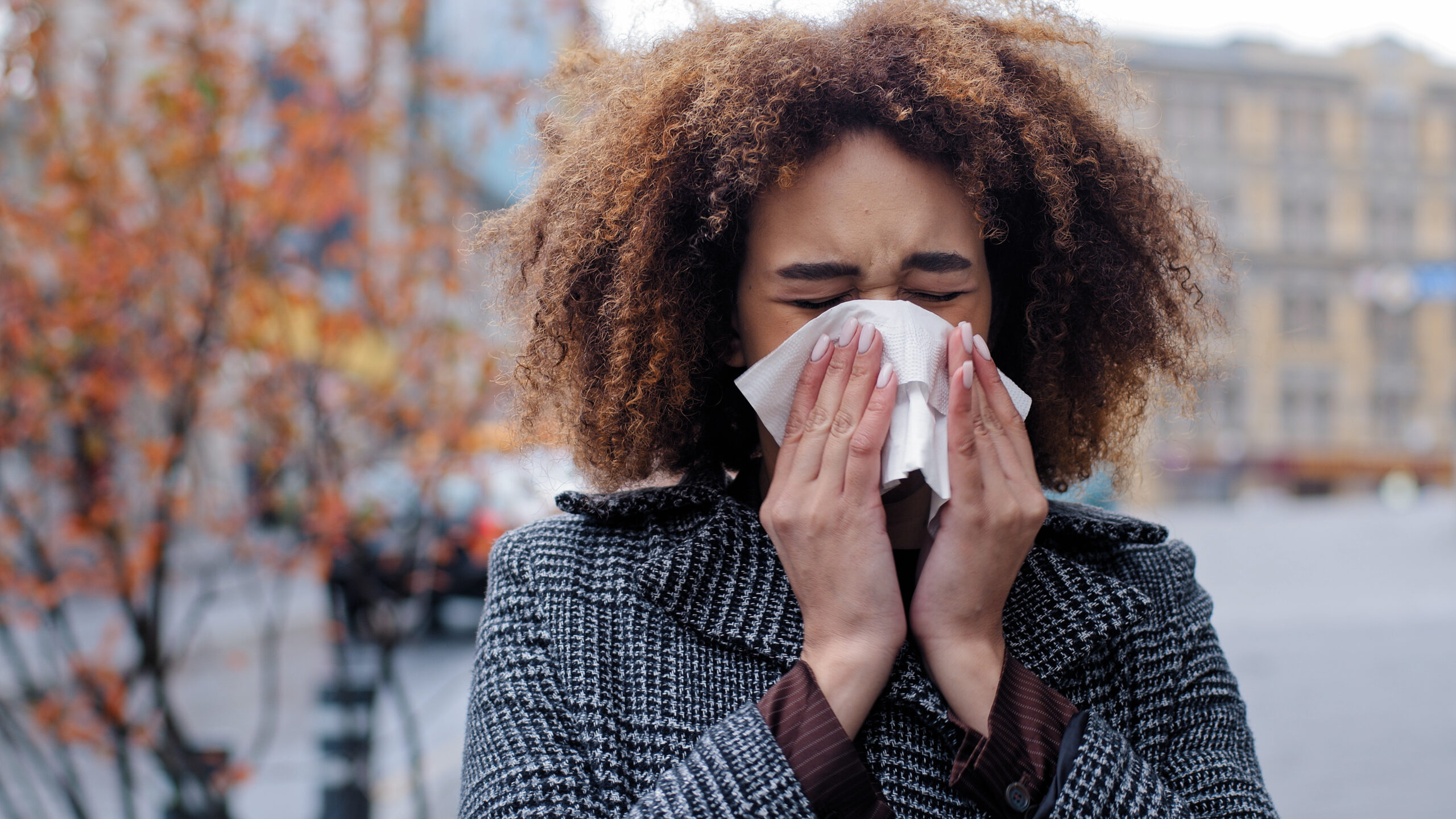Woman sneezing into white tissue trying not to pee when she sneezes - peeing when I sneeze